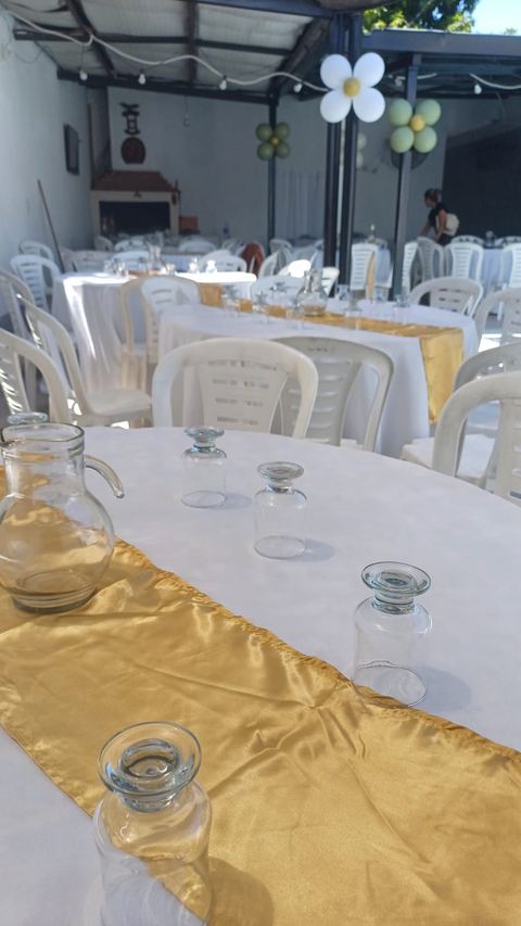 Mesas del patio techado montadas con mantelería y camino dorado para un evento